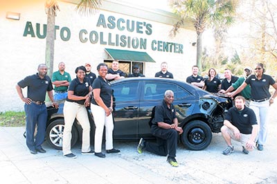 Ascue's Auto Collision Center Staff posing by a wrecked car